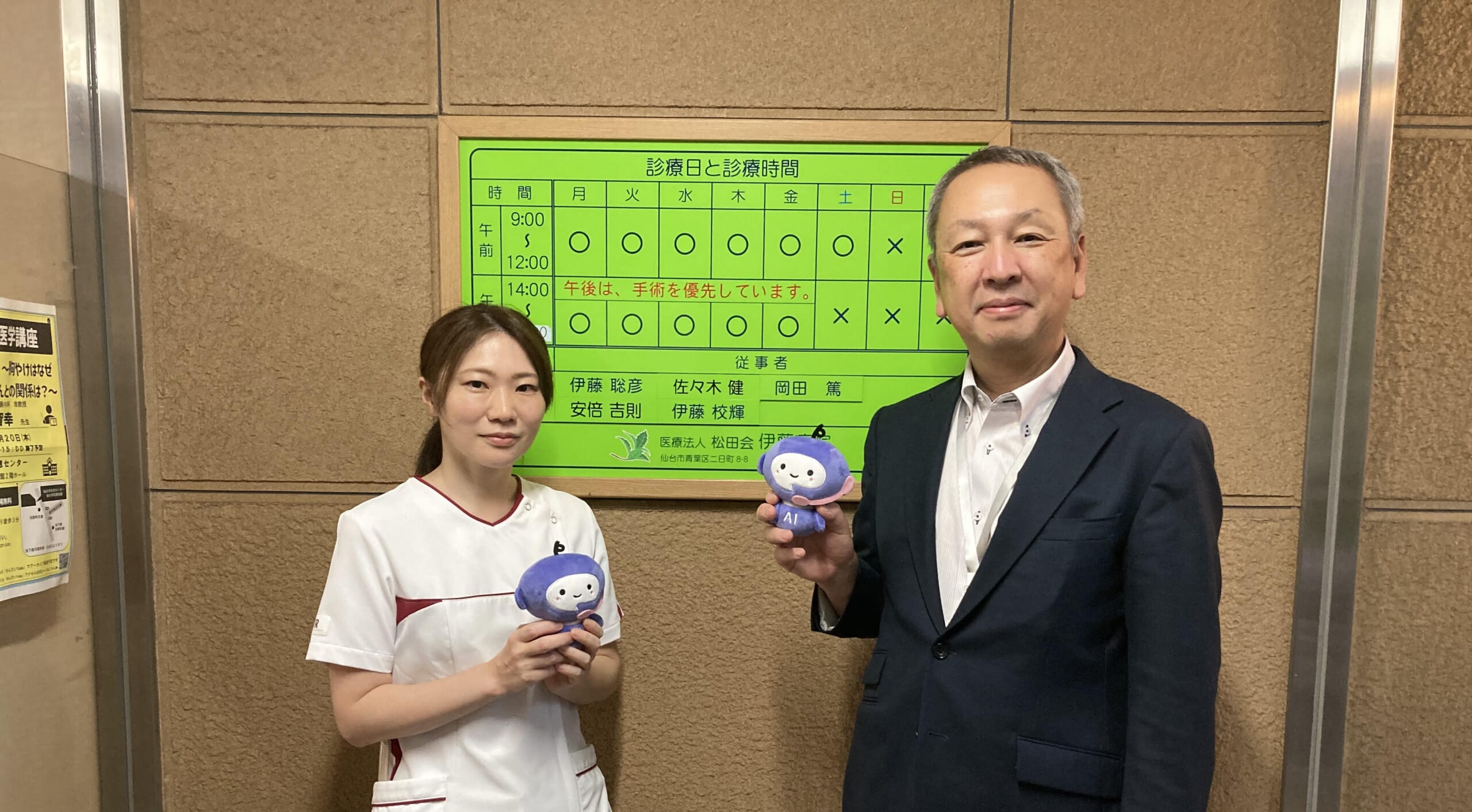 医療法人松田会 伊藤病院の看板前。左側が副看護師長の小菅さん、右側が事務部の佐竹さん